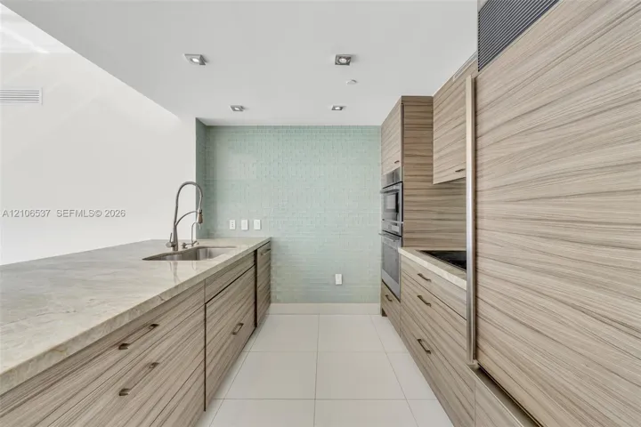 Kitchen featuring horizontal wood-grain cabinetry, stone countertops, integrated stainless steel appliances, a tile backsplash, and recessed lighting