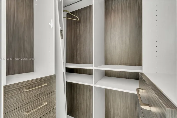 Custom closet organization system featuring wood-finish cabinetry, adjustable shelving, integrated drawer storage, and satin-finish metal hardware