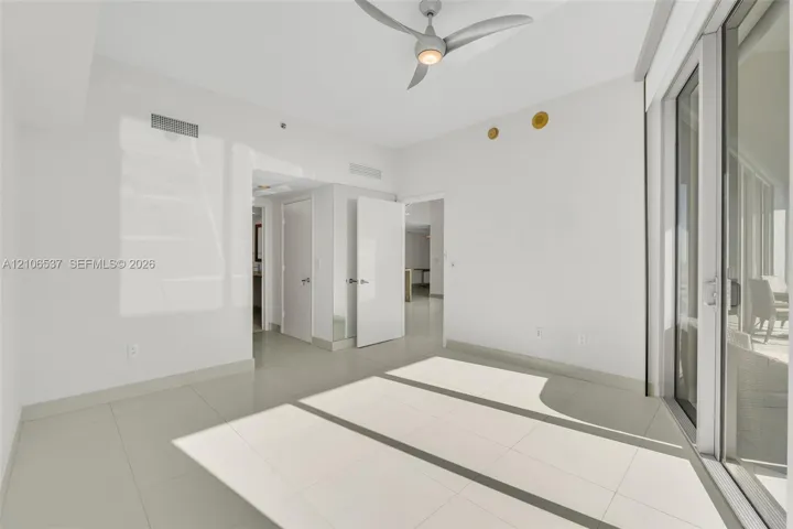 Neutral-toned interior featuring large-format tile flooring, a modern multi-blade ceiling fan, and expansive floor-to-ceiling glass sliding doors