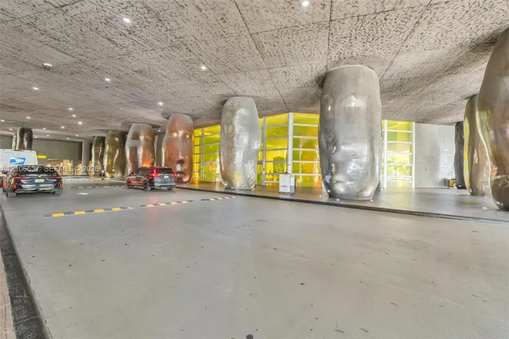 Covered porte-cochère featuring a textured concrete ceiling, recessed lighting, and sculptural metallic columns