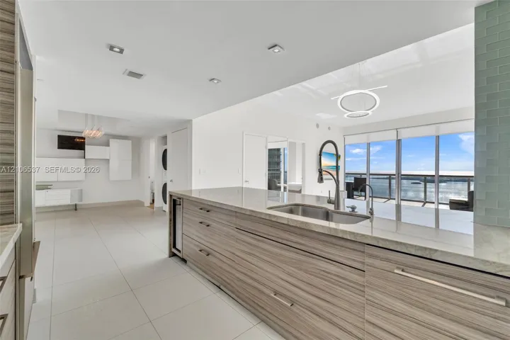 Kitchen featuring flat-panel wood-finish cabinetry, stone countertops, stainless steel undermount sink with a pull-down faucet, large-format tile flooring, and floor-to-ceiling windows