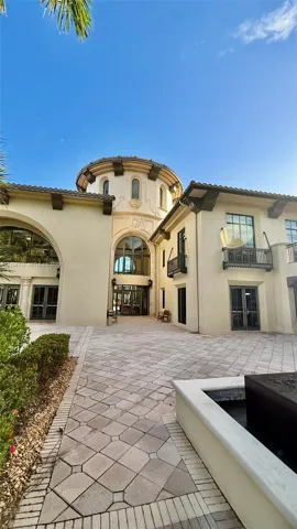 Stucco exterior featuring a prominent rotunda, arched entryway, decorative corbels, metal-railing balconies, and a paved courtyard with a stone water feature