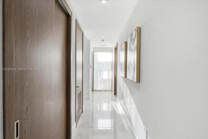 Hallway featuring polished tile flooring, recessed ceiling lighting, and wood-finish doors with integrated hardware