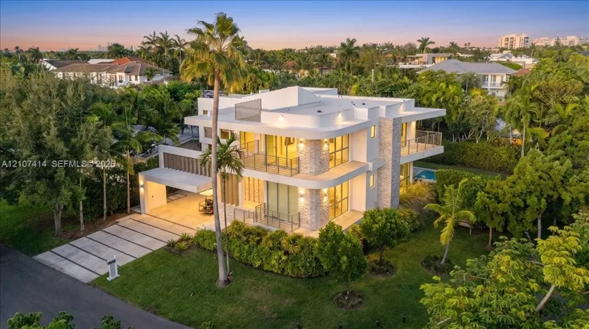 Multi-level modern exterior featuring stone cladding, expansive floor-to-ceiling glass windows, multiple wrap-around balconies, and a concrete paver driveway