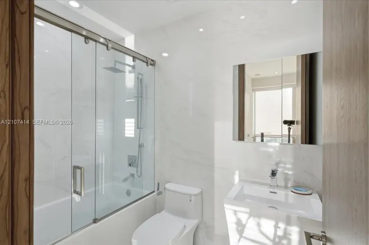Bathroom featuring full-height stone-finish wall tile, a glass-enclosed shower with a rainfall showerhead, a wall-mounted medicine cabinet, and a contemporary pedestal sink with a chrome faucet