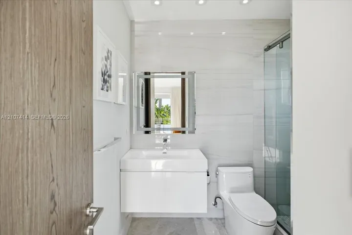 Modern bathroom featuring a white floating vanity with a vessel sink, integrated LED-lit mirror, glass-enclosed shower, and stone-finish floor tiling