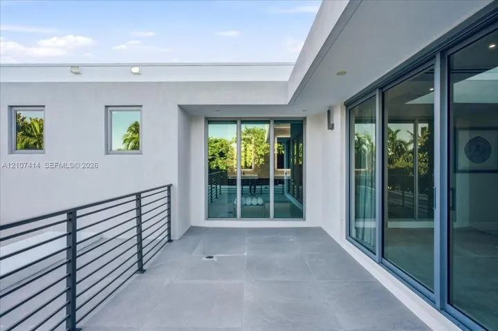 Modern balcony featuring expansive stone-tile flooring, floor-to-ceiling glass sliding doors, and a sleek metal horizontal-bar railing