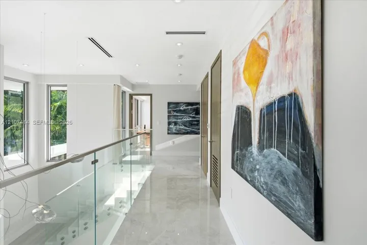 Hallway featuring polished tile flooring, a glass panel railing with metallic hardware, recessed ceiling lighting, and solid wood-finish doors