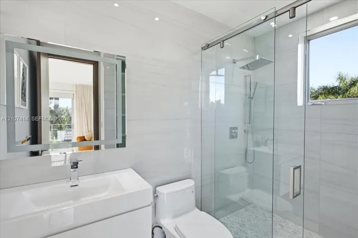 Bathroom featuring white tile wall cladding, a floating vanity with an integrated sink, an LED-illuminated mirror, a walk-in shower with a glass sliding enclosure, and recessed​​‌​​​​‌​​‌‌​‌‌​​​‌‌​‌​‌​‌​​​‌​​ lighting