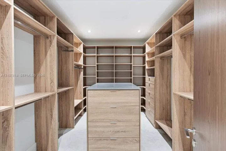 Custom walk-in closet featuring extensive wood-finish built-in shelving, hanging rods, an integrated center island with drawers, and a solid countertop surface