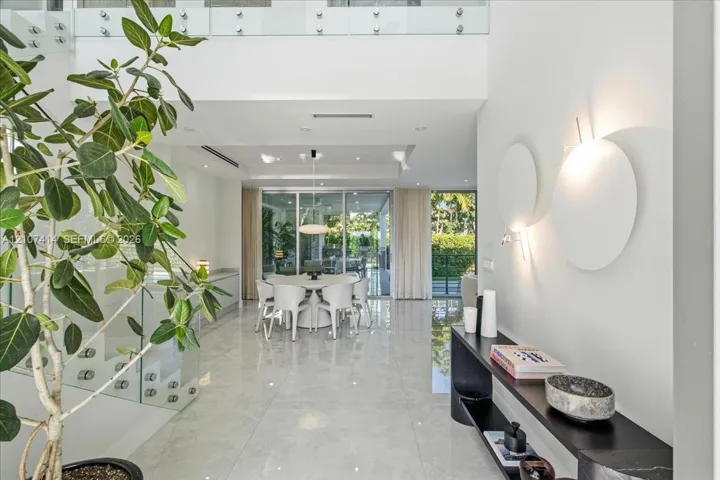 Double-height entryway featuring polished tile flooring, glass-panel staircase railing, recessed lighting, and wall-mounted circular accent fixtures