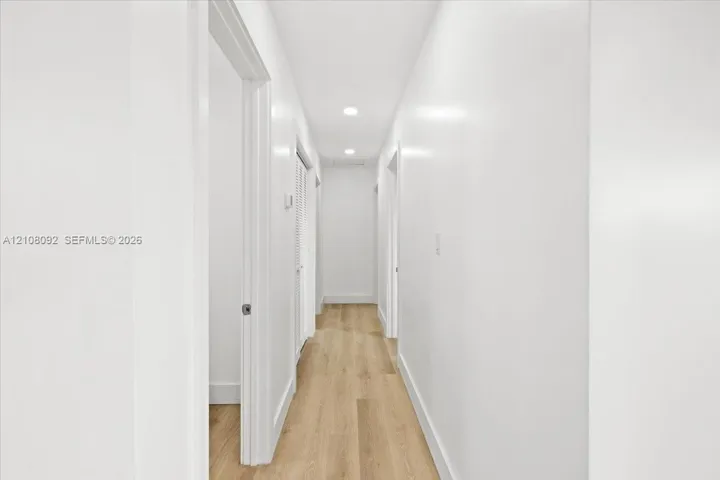 Hallway featuring wood-finish flooring, crisp white walls, recessed ceiling lighting, and louvered closet doors