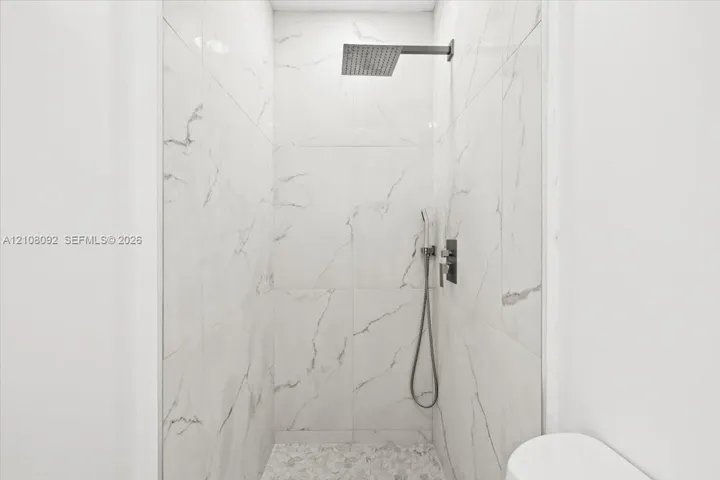 Walk-in shower featuring floor-to-ceiling large-format tile, wall-mounted rain shower head, handheld shower fixture, and stone-finish floor tile