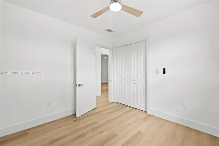 Room featuring wood-finish flooring, white walls, double-door closet, and an integrated ceiling fan with light fixture