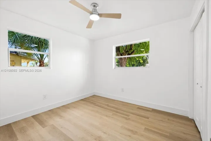 Interior space featuring wood-finish flooring, two dual-pane windows, a ceiling fan with integrated lighting, and a closet with bifold doors