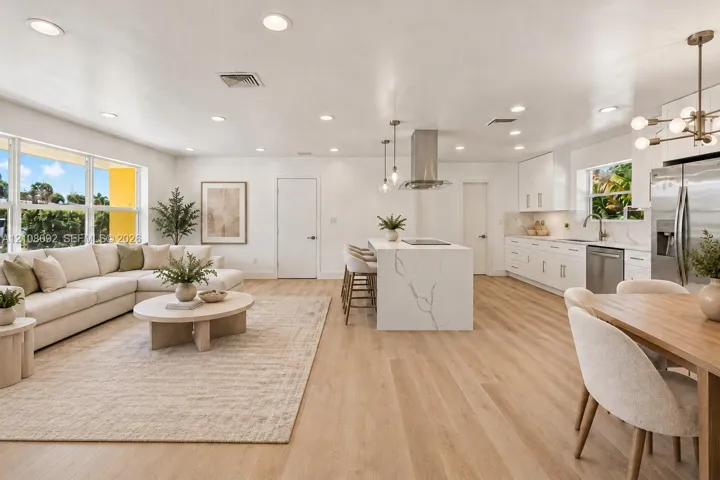 AI Image Open-concept kitchen and living area featuring wood-finish flooring, a waterfall-edge kitchen island, stainless steel range hood, recessed lighting, and large windows