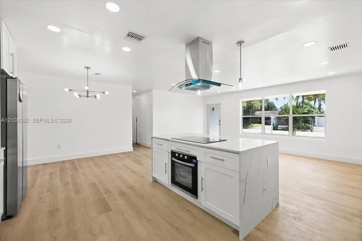 Kitchen featuring a central island with a stone-finish countertop and built-in electric cooktop, stainless steel chimney-style range hood, recessed ceiling lighting, and wood-finish flooring