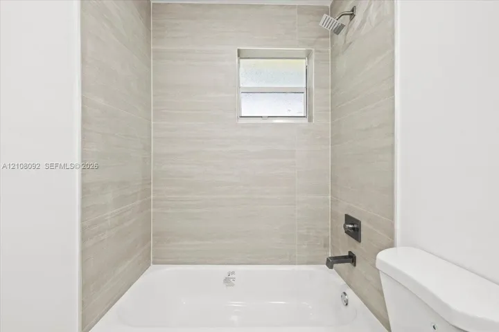 Bathtub with horizontal tile surround, square fixed-pane window, and matte black plumbing fixtures including a rainfall showerhead