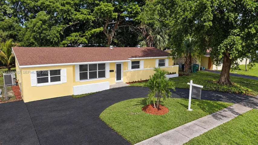 Single-story residence featuring a paved curved driveway, multi-pane windows with white exterior shutters, and mature trees