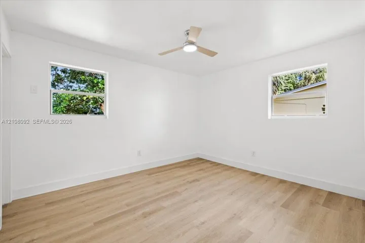 Bright room featuring wood-finish flooring, dual windows, and an integrated ceiling fan with light fixture