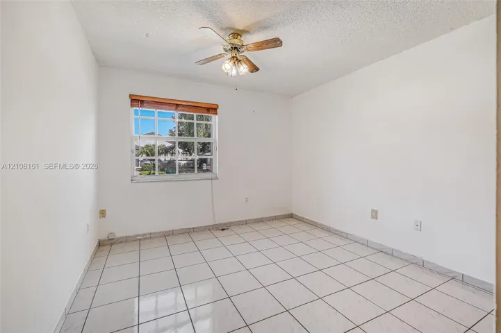 Interior space featuring light-toned tile flooring, a multi-pane window with wood-finish blinds, and a centrally mounted ceiling fan with integrated lighting