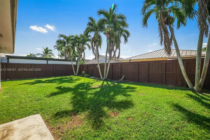 Backyard featuring a grass lawn, perimeter wood fencing, and established palm trees
