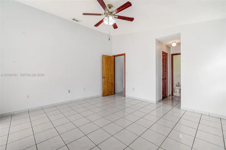 Spacious room featuring vaulted ceilings, light-toned ceramic tile flooring, a multi-blade ceiling fan with integrated lighting, and wooden door finishes