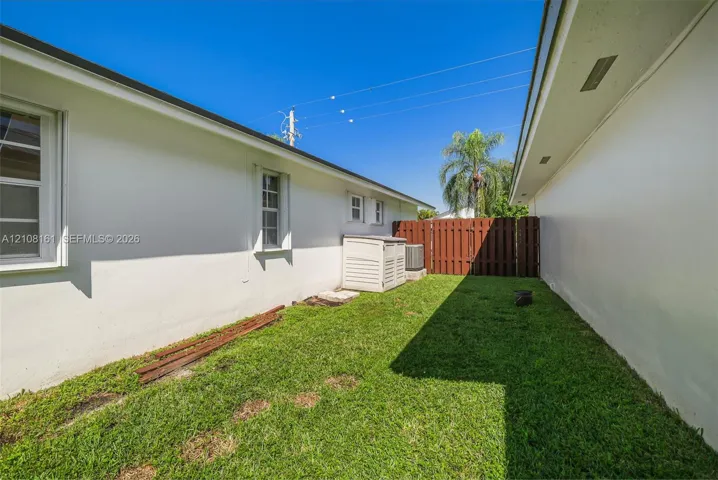 Side yard featuring white stucco exterior walls, a grass lawn, and a solid wood privacy fence