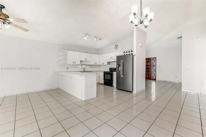 Kitchen featuring white cabinetry, a peninsula, tile flooring, stainless steel refrigerator, and vaulted ceilings with multi-light fixture