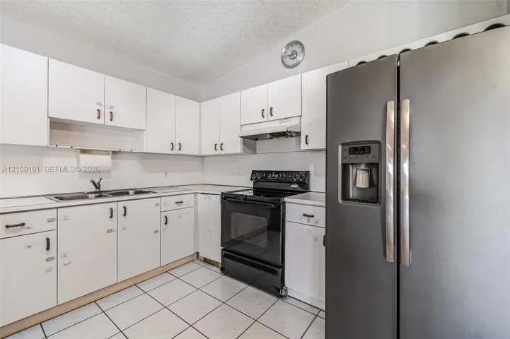 Kitchen featuring white cabinetry, stainless steel appliances, a dual-basin sink, and tile flooring
