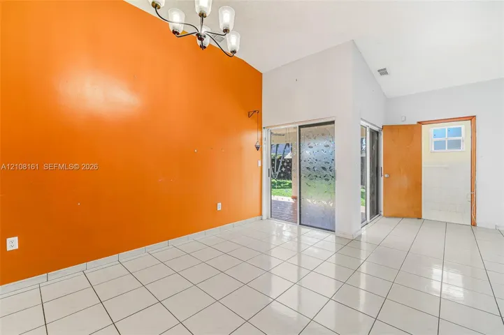 High-ceiling interior space featuring large-format ceramic tile flooring, a multi-arm chandelier, sliding glass doors with frosted glass detailing, and a solid wood entry door