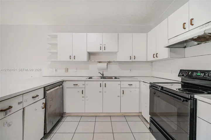 Kitchen featuring white cabinetry, solid-surface countertops, dual-basin stainless steel sink, tile flooring, and integrated black appliance suite