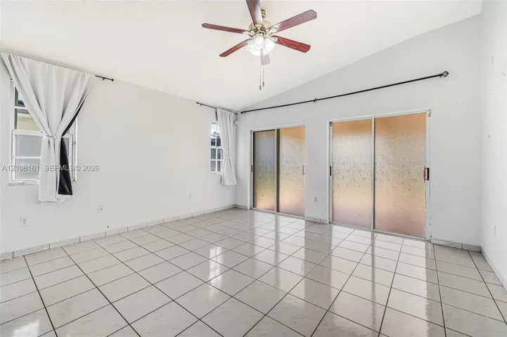 Vaulted ceilings, large-format tile flooring, dual sets of sliding glass doors, and a central ceiling fan with integrated lighting