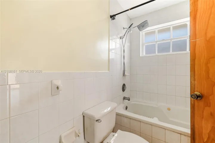 Bathroom featuring white tile wall surround, soaking tub, adjustable shower head, and a rectangular window