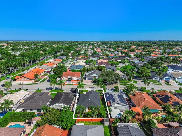 Aerial perspective of a single-family residence featuring a dark shingle roof, a landscaped backyard, and a fenced perimeter
