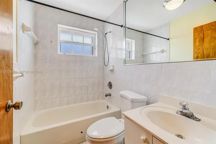 Bathroom featuring full-height wall tile, a standard tub and shower combination with chrome fixtures, a white vanity with an integrated sink, and a large-format vanity mirror
