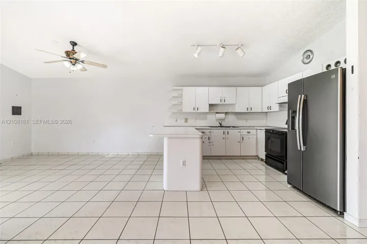 Kitchen featuring white cabinetry, an island with an extended countertop, large-format tile flooring, a stainless steel side-by-side refrigerator, and track lighting