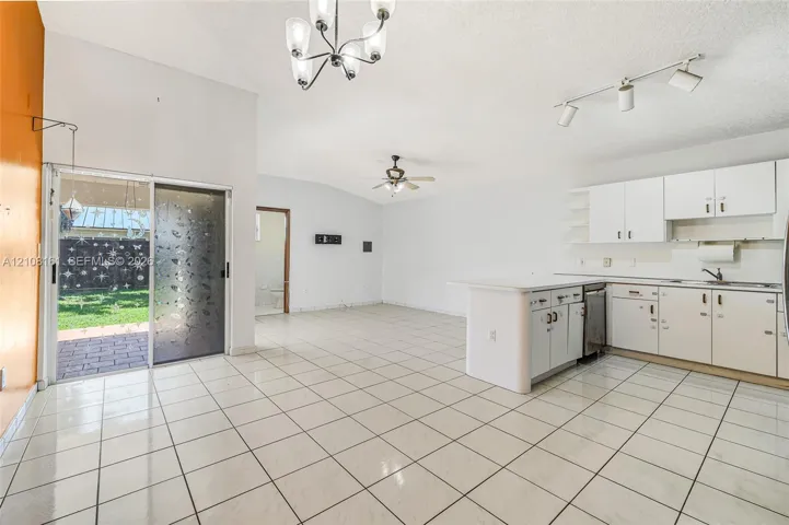 Open-concept kitchen featuring a center island, white cabinetry, tile flooring, sliding glass door, and vaulted ceilings with multi-bulb fixtures