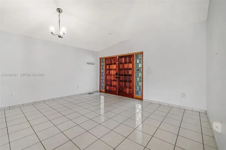 Entryway featuring ceramic tile flooring, vaulted ceilings, dual wood-finish doors, glass block sidelights, and a tiered metal chandelier