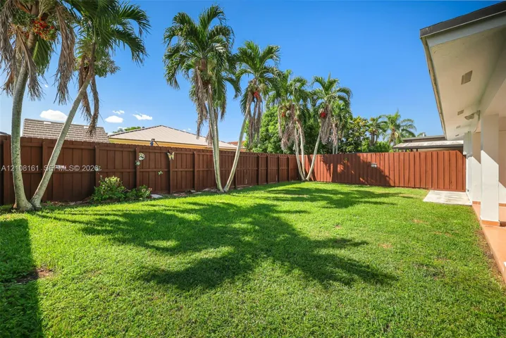 Rear yard featuring a manicured lawn, mature palm trees, and a full-perimeter privacy fence