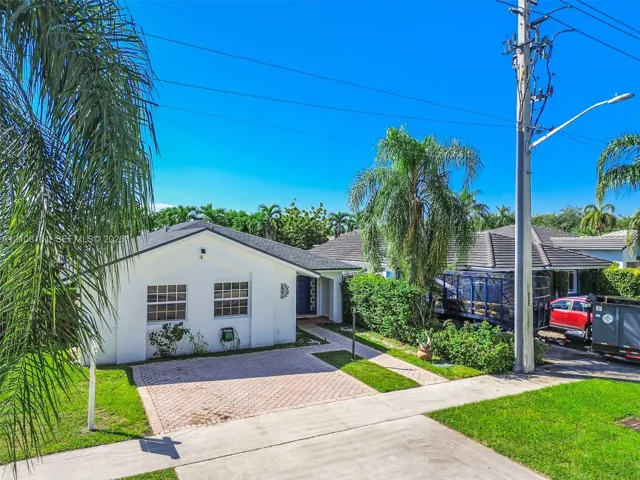 Single-story residence featuring a white stucco exterior, multi-hipped roof, paved driveway, and established landscape