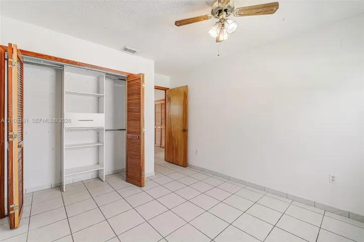 Room featuring ceramic tile flooring, a dual-door closet with built-in shelving, a natural wood-finish interior door, and a multi-light ceiling fan