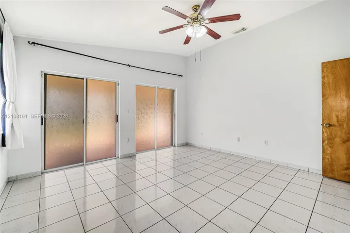 Vaulted ceiling featuring a central ceiling fan with integrated lighting, polished tile flooring, and dual sliding glass doors