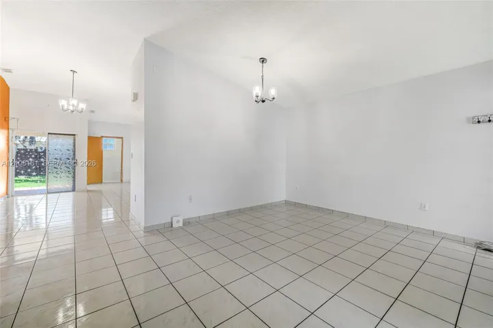 Interior space featuring light-colored tile flooring, neutral walls, two decorative multi-light chandeliers, and sliding glass door access to the exterior