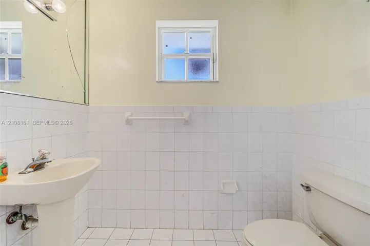 Bathroom featuring a pedestal sink with a chrome faucet, white square-tile wainscoting, a multi-pane fixed window, and a built-in ceramic soap dish