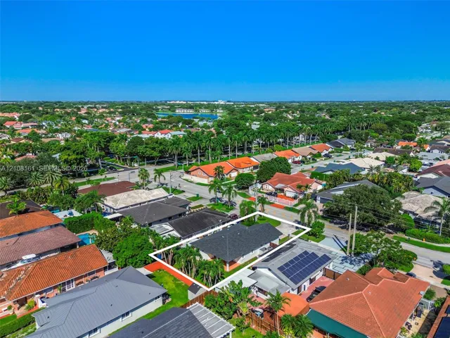 Aerial perspective of a residential lot featuring a multi-hipped roofline, mature palm trees, and fenced perimeter