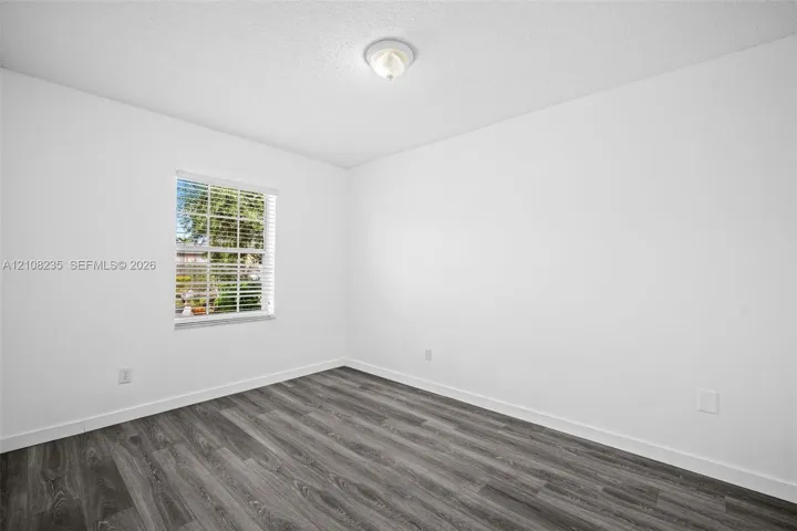 Room featuring wood-finish flooring, white walls, and a window with horizontal blinds
