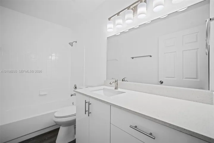 Bathroom featuring a white vanity cabinet, solid surface countertop with an integrated basin, full-width vanity mirror, five-light fixture, and a tub-shower combination with tile surround