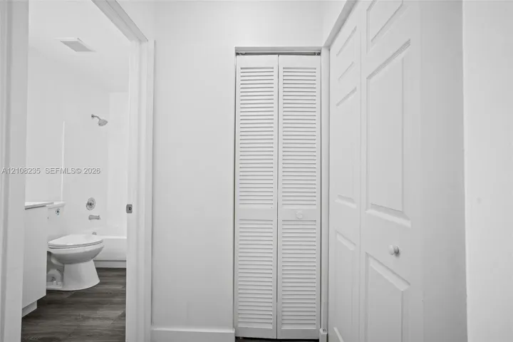 White bifold louvered closet doors, dual-panel interior doors, and wood-finish flooring