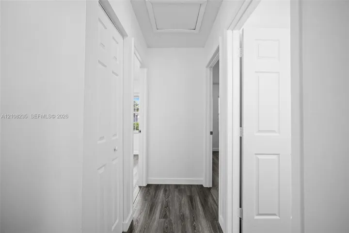 Hallway featuring wood-finish flooring, six-panel interior doors, and a ceiling access panel